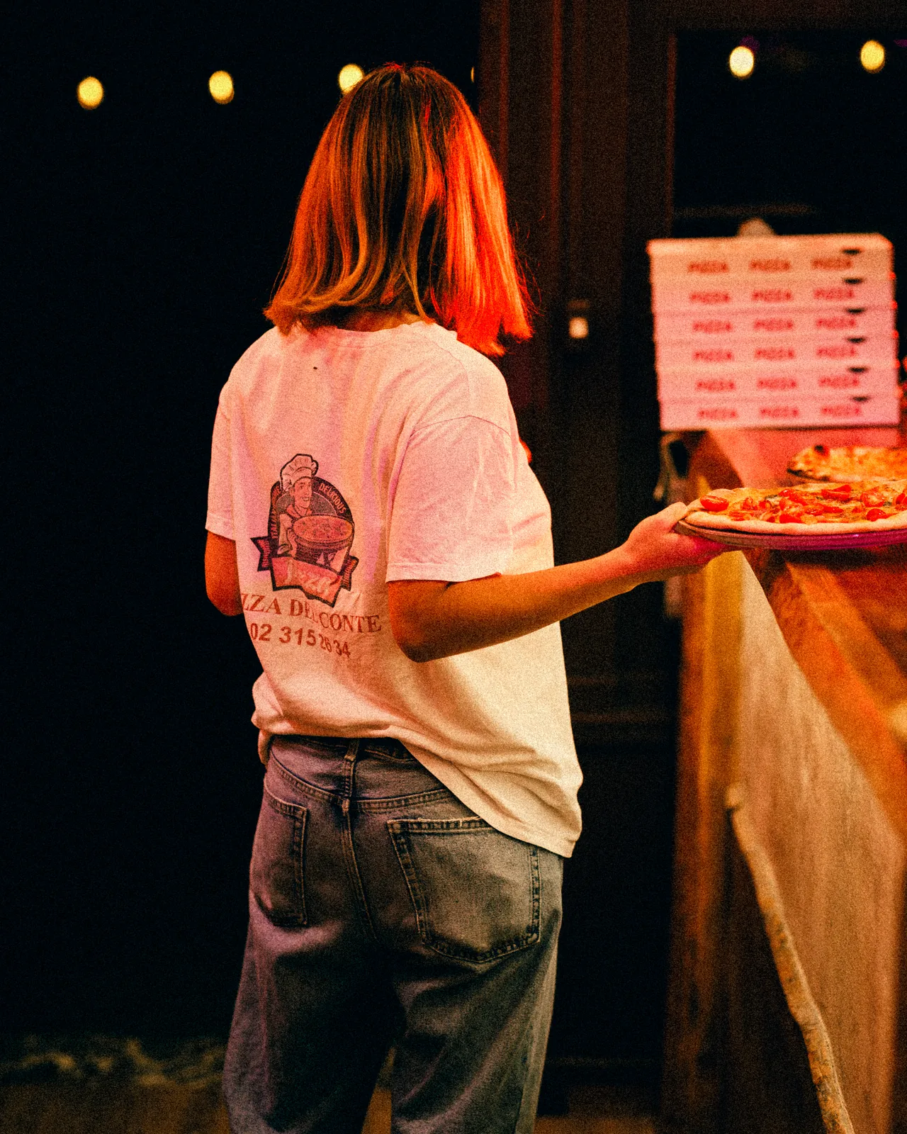 Une serveuse emporte une pizza, logo Pizza Del Conte au dos